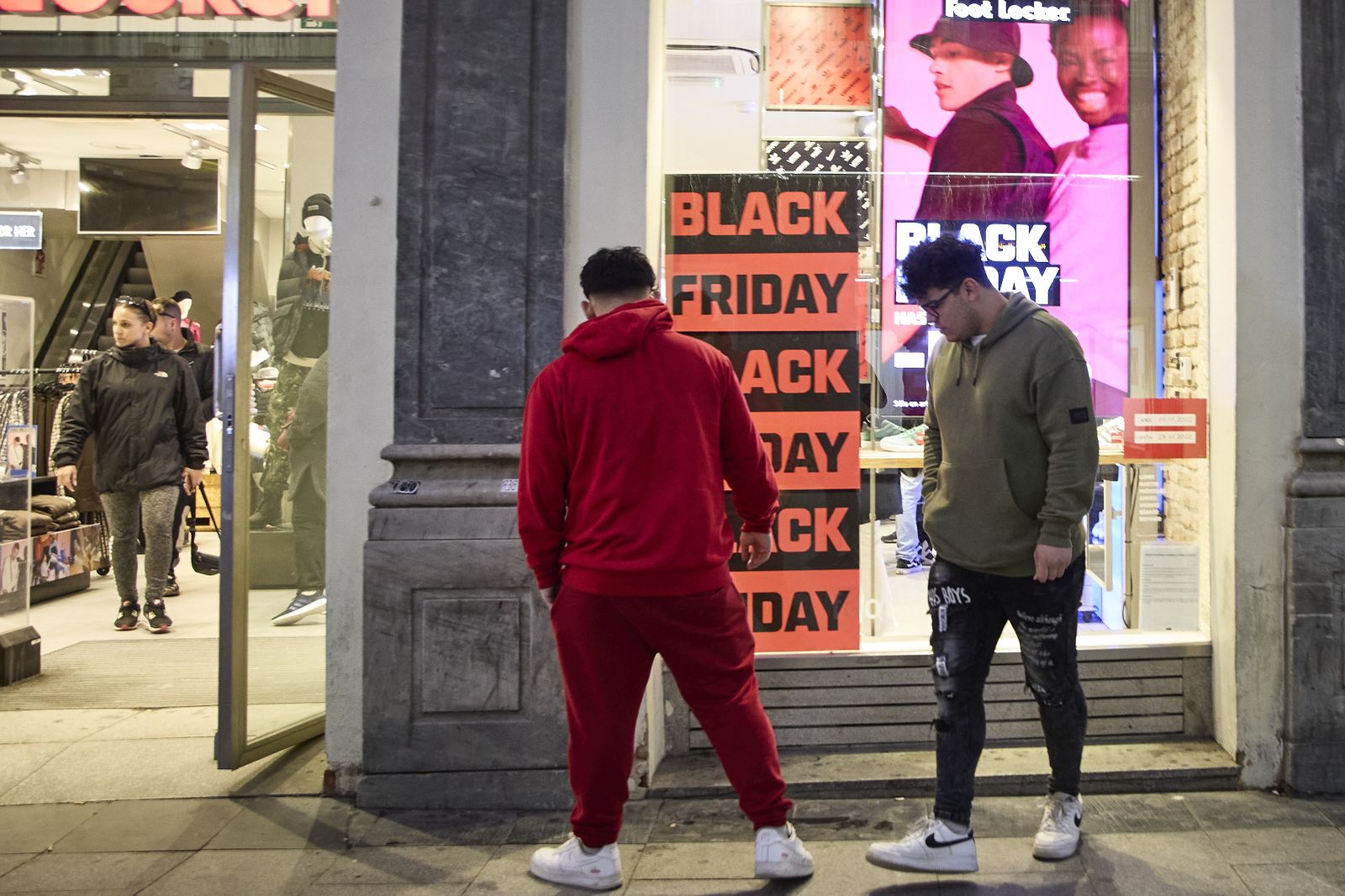 Varias personas pasan por delante de los comercios que anuncian los descuentos del Black Friday
