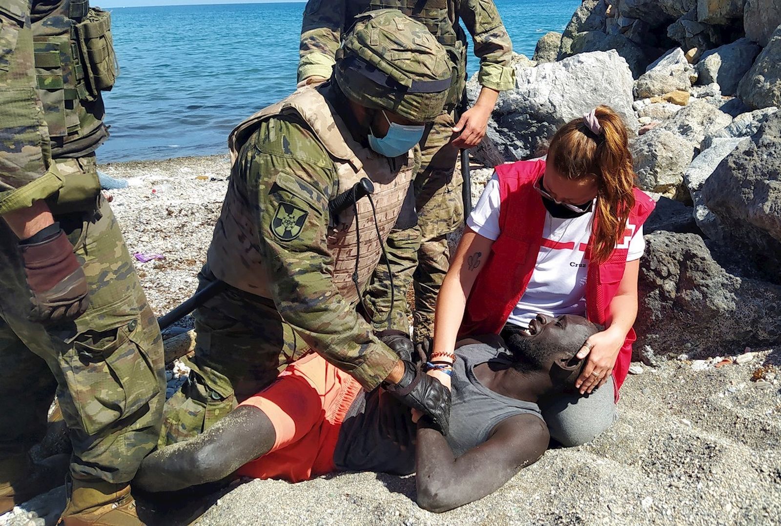 La voluntaria de Cruz Roja Luna Reyes y miembros del Ejército de Tierra atienden a un migrante llegada a Ceuta