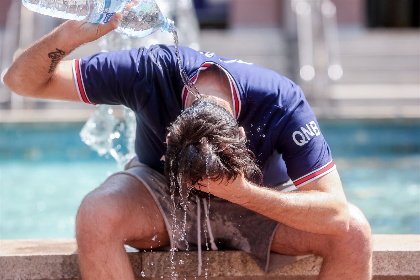 Un joven se tira una botella de agua por encima para combatir la segunda ola de calor en Madrid, en verano de 2022