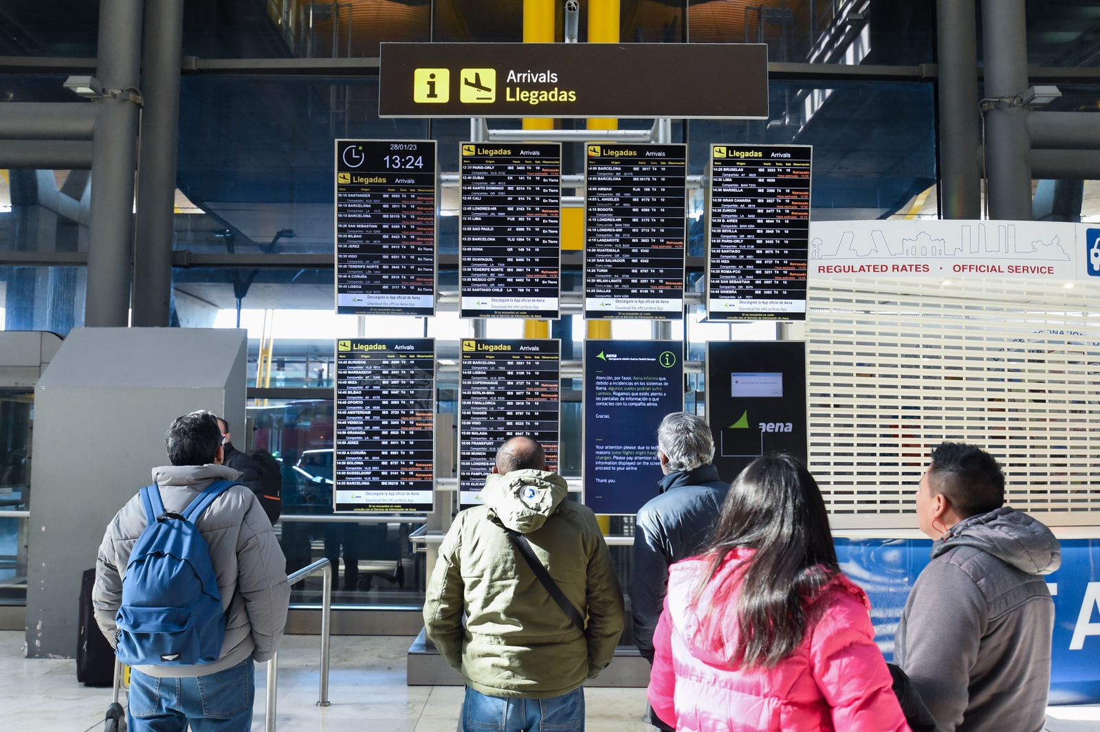 Varias personas observan los paneles informativos que anuncian retrasos de llegadas en algunos vuelos de Iberia en la Terminal 4