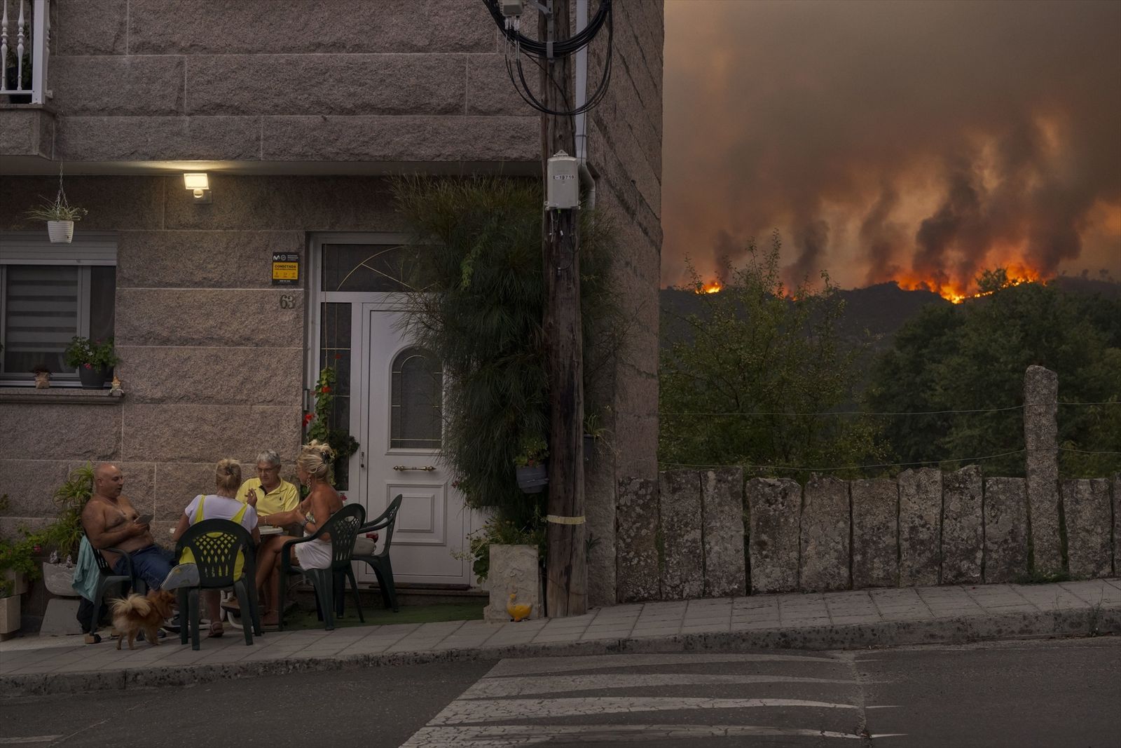 Un grupo de personas juega a las cartas mientras avanza el incendio forestal en Carballeda de Avia, Galicia, noroeste de España