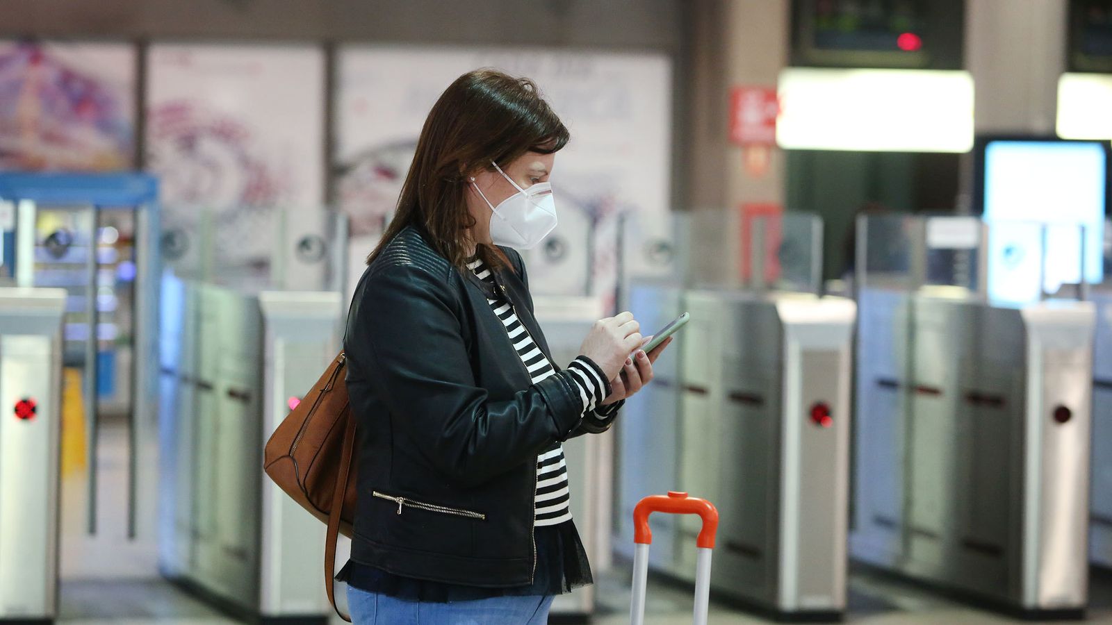 Una viajera con mascarilla consulta su móvil en la estación de Atocha