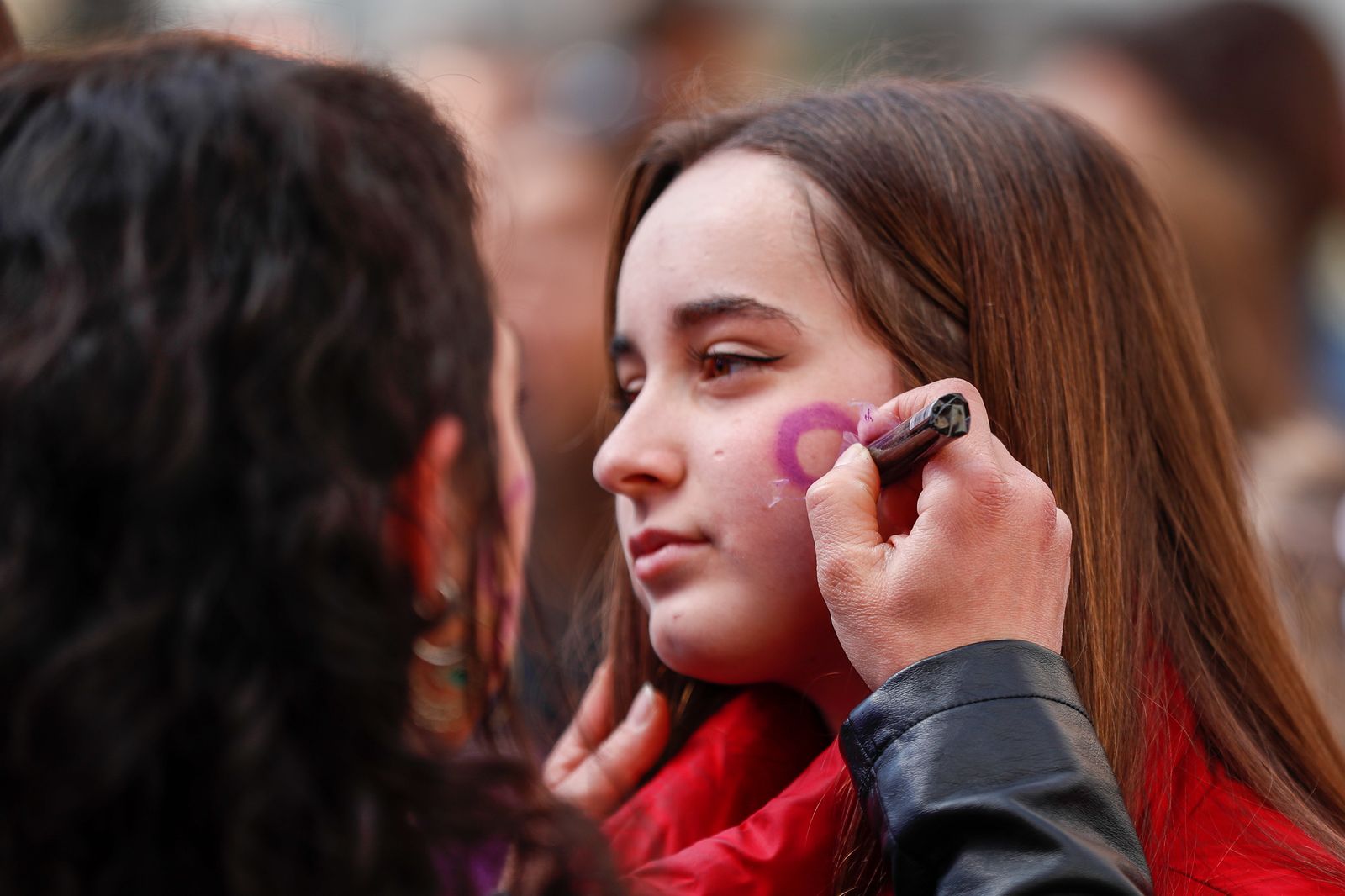 Una mujer pinta la cara de una joven con el símbolo de la mujer