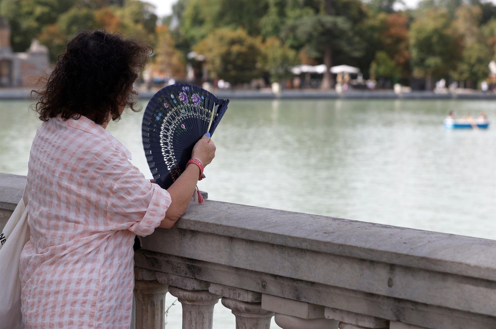 Quien tiene un abanico, tiene un tesoro. Imprescindible en estos días de ola de calor. Esta mujer aprovecha y usa el suyo en Madrid, mientras contempla a los valientes que reman bajo el ardiente sol en el lago del Retiro.