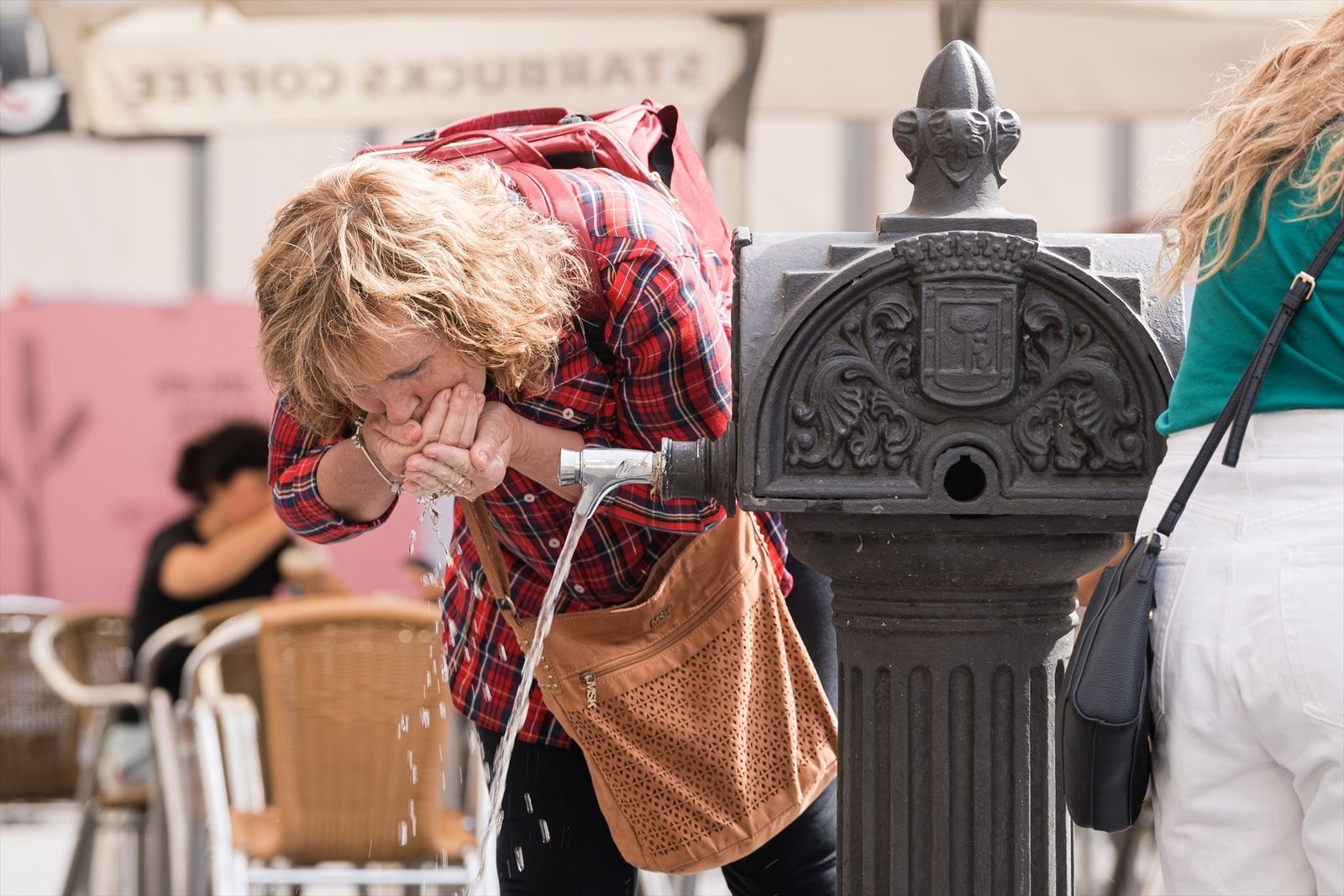 Una mujer bebiendo de una fuente en Madrid