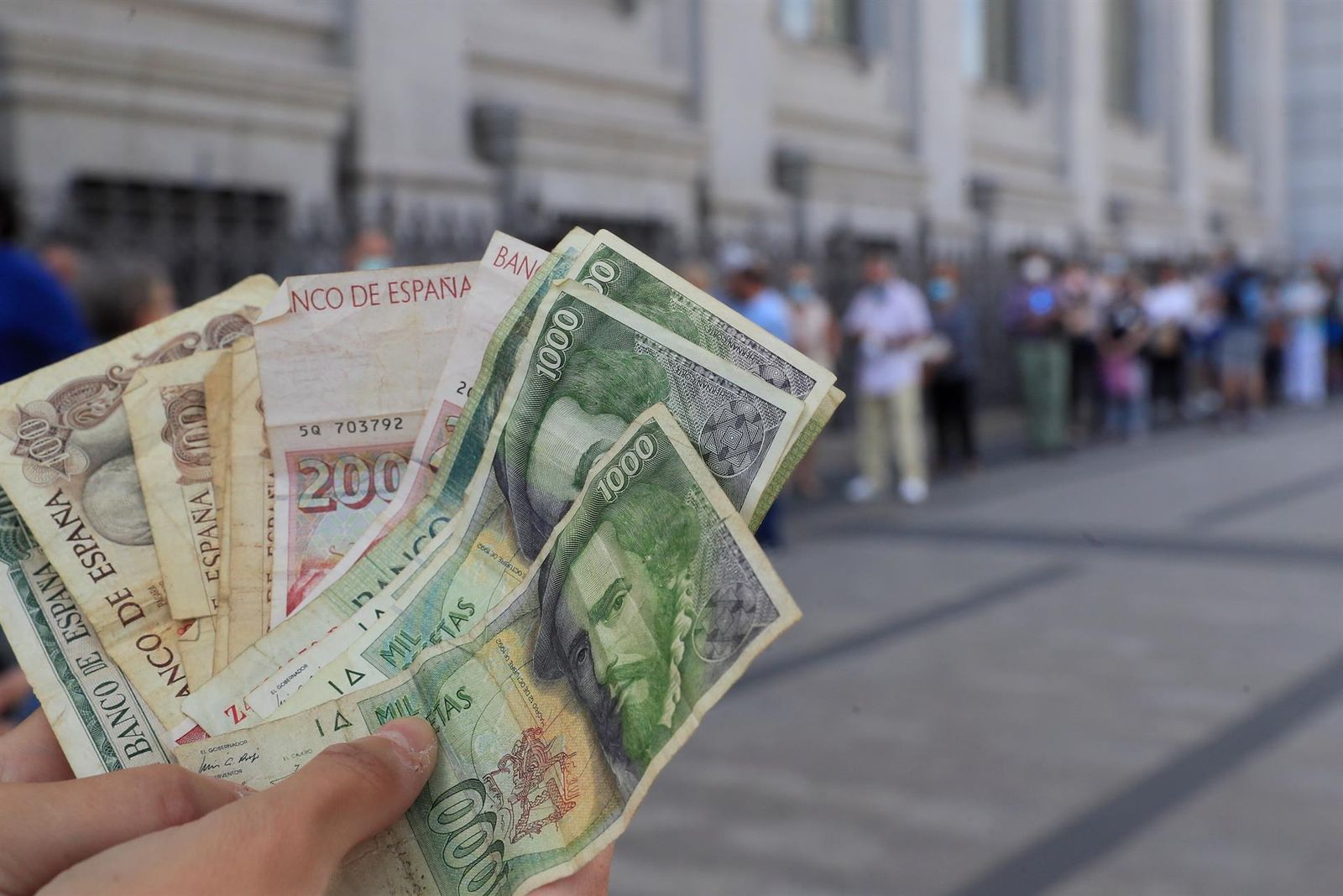 Una persona muestra sus pesetas ante la fila de quienes aguardan para canjear las suyas en el Banco de España