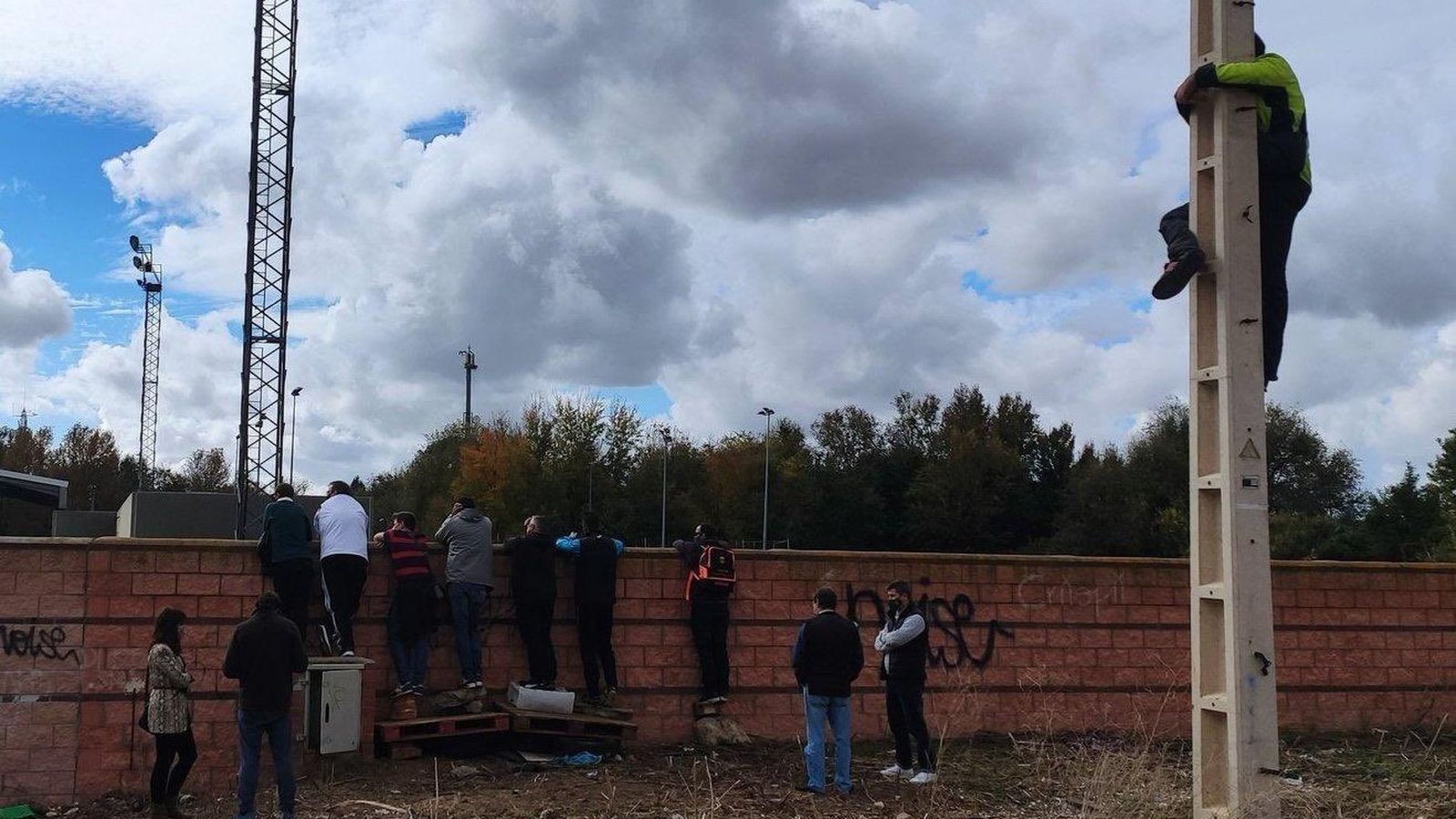 Padres tras un muro y uno suido a un poste de la luz