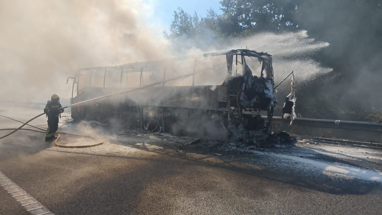 Un bombero refresca un autobús calcinado