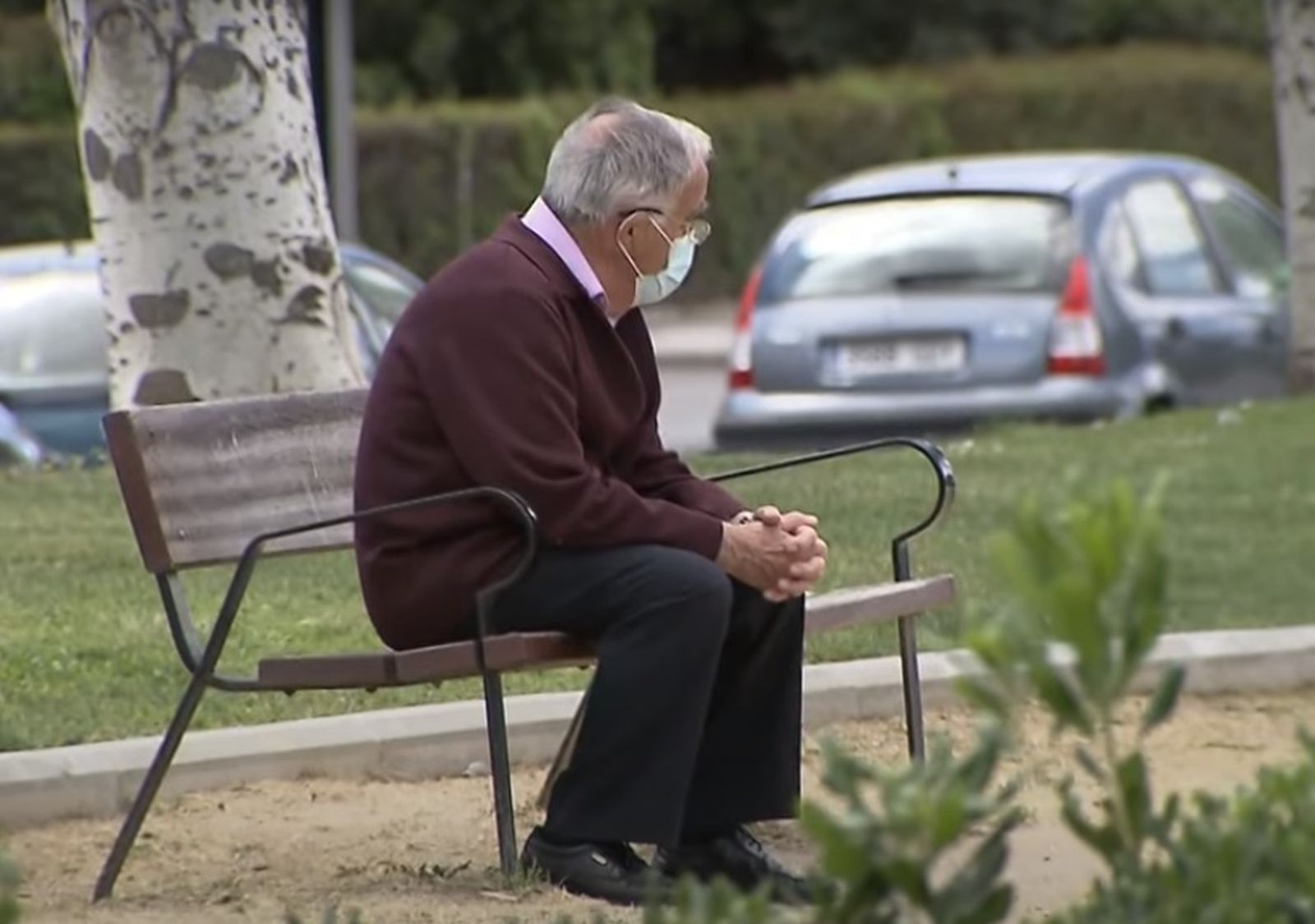 Una persona mayor descansa en un banco de la calle