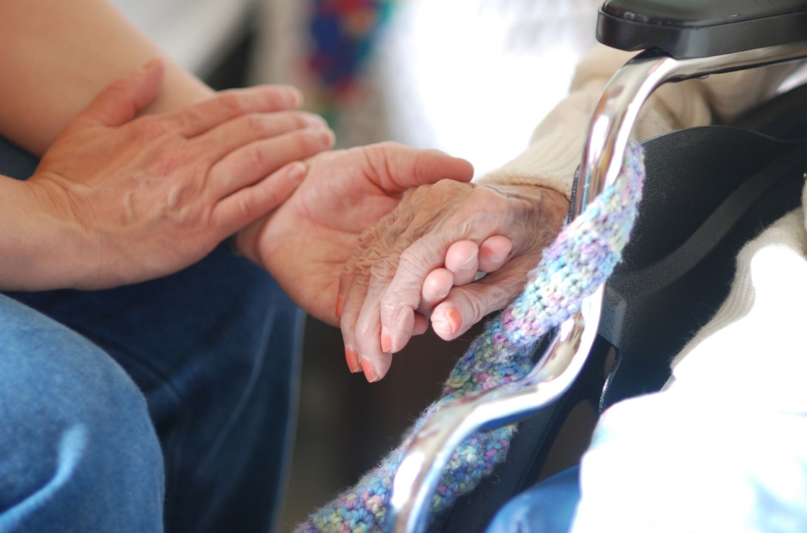 Una persona sostiene la mano a una mujer mayor en silla de ruedas