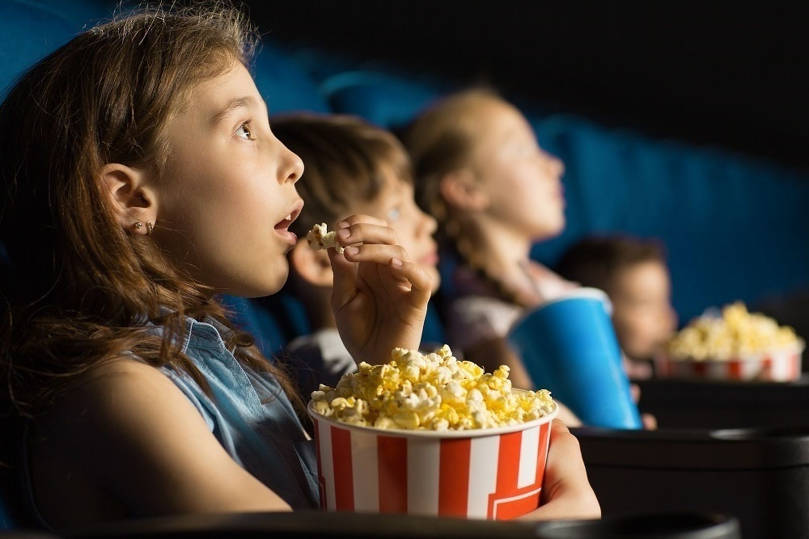Unos niños comen palomitas mientras ven una película en una sala de cine
