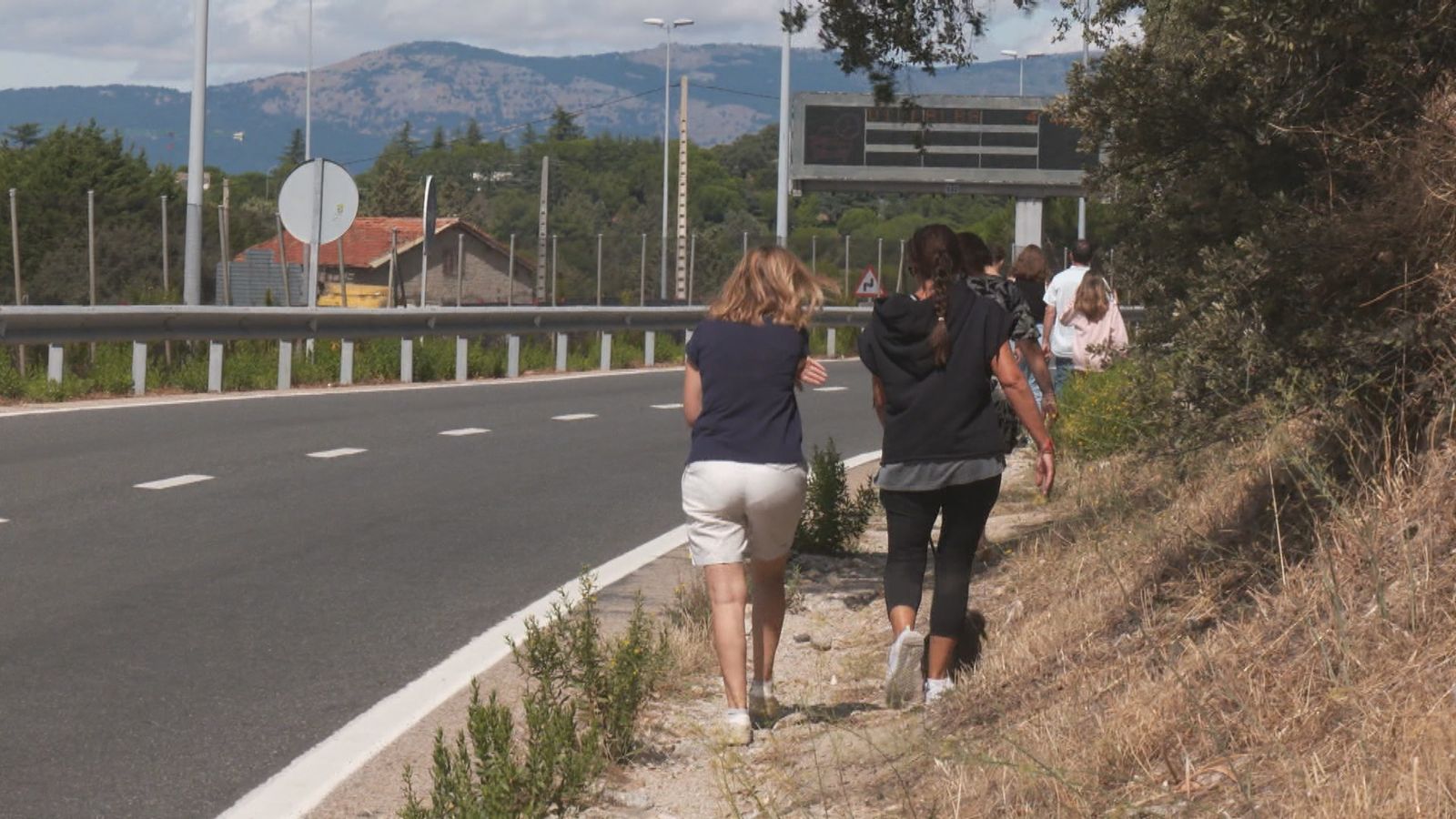 Personas caminan cerca de la vía de servicio de la A-6, en Torrelodones