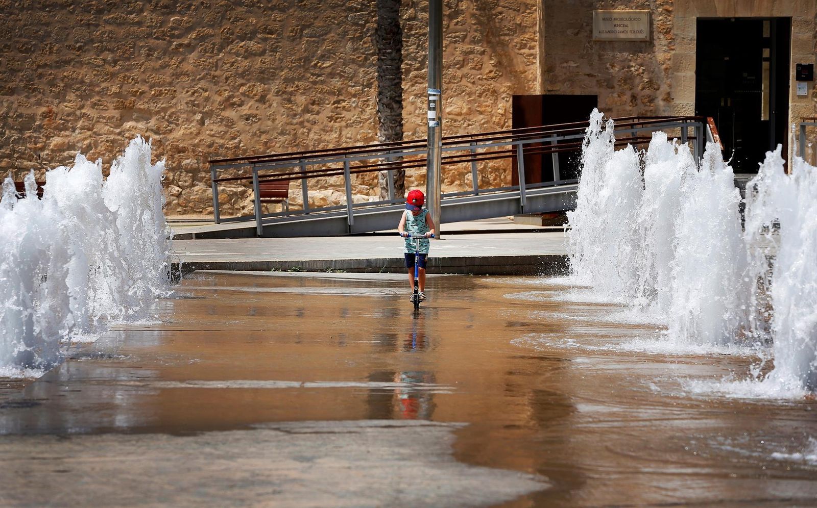 Un niño busca la mejor zona de juego en Alicante, rodeado por chorros de agua. Allí las temperaturas serán algo más benévolas, aunque 33 grados en la costa ya es mucho calor...