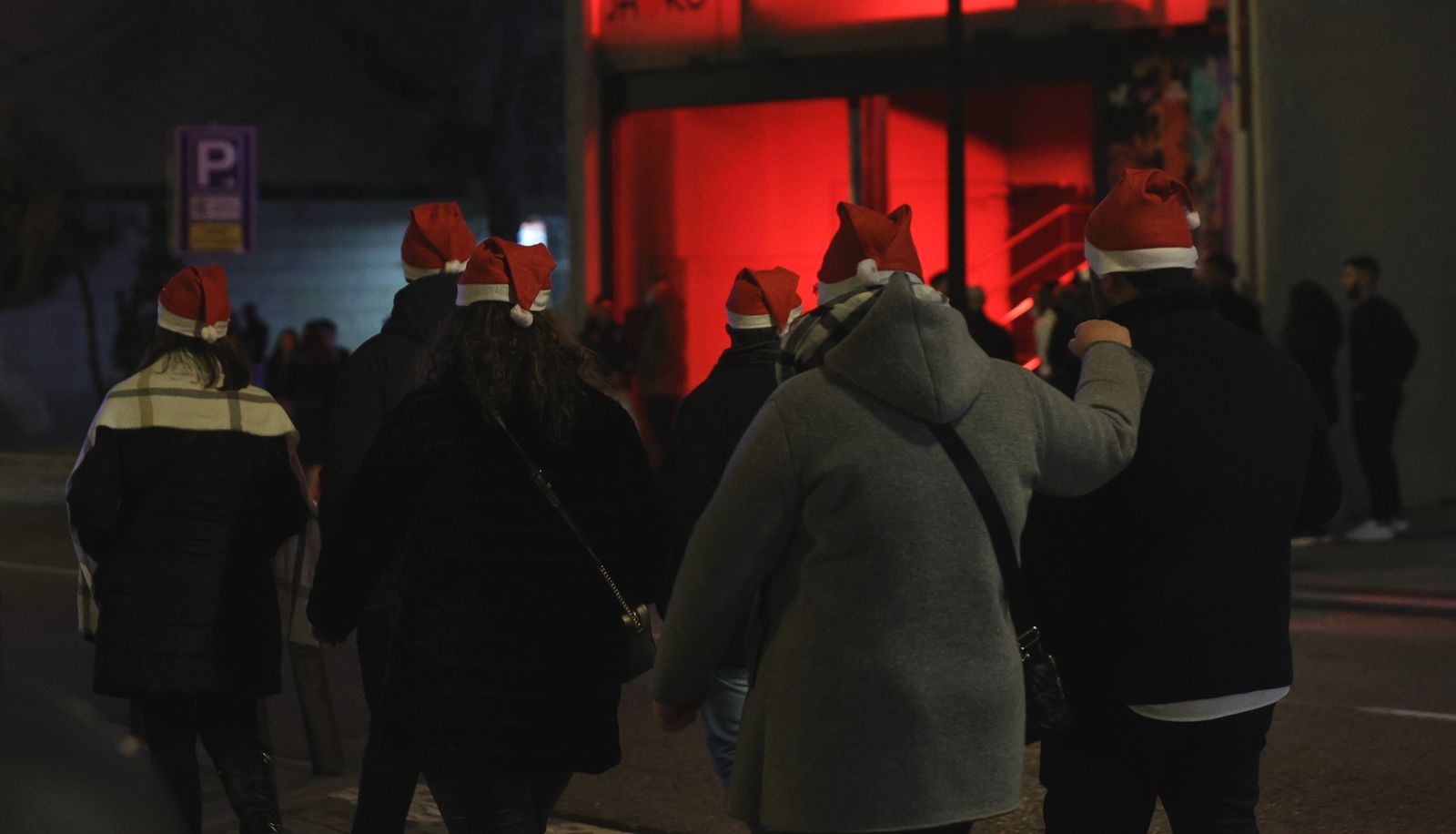 Un grupo de personas pasa por delante de una cola de gente que espera para entrar a una fiesta de Nochevieja