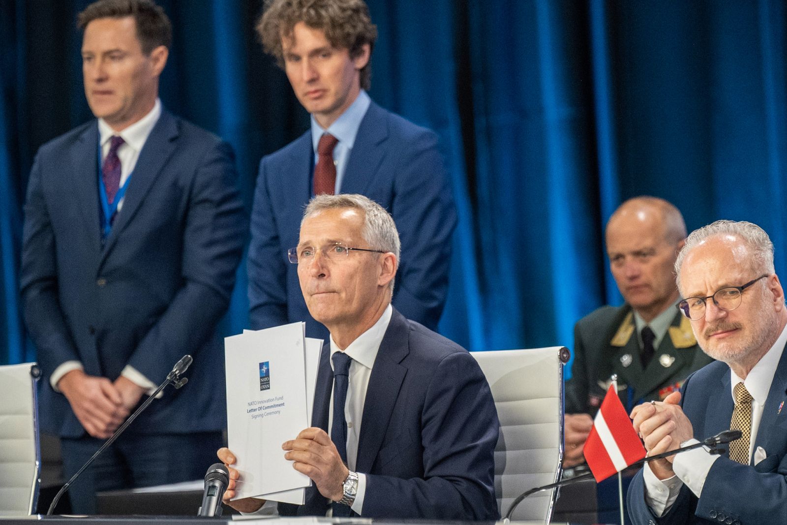 El Secretario General de la OTAN, Jens Stoltenberg (C), sostiene la Carta de compromiso del Fondo de Innovación de la OTAN durante la ceremonia de firma.