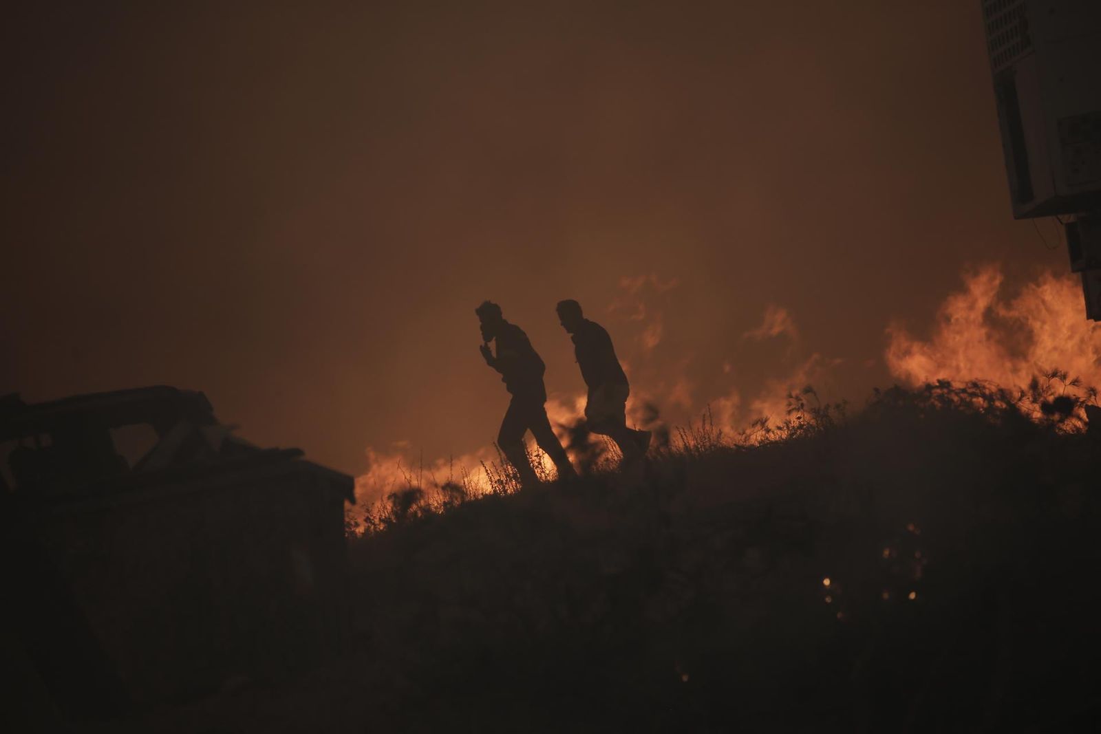 Dos personas caminan cerca de las llamas en uno de los incendios de Grecia