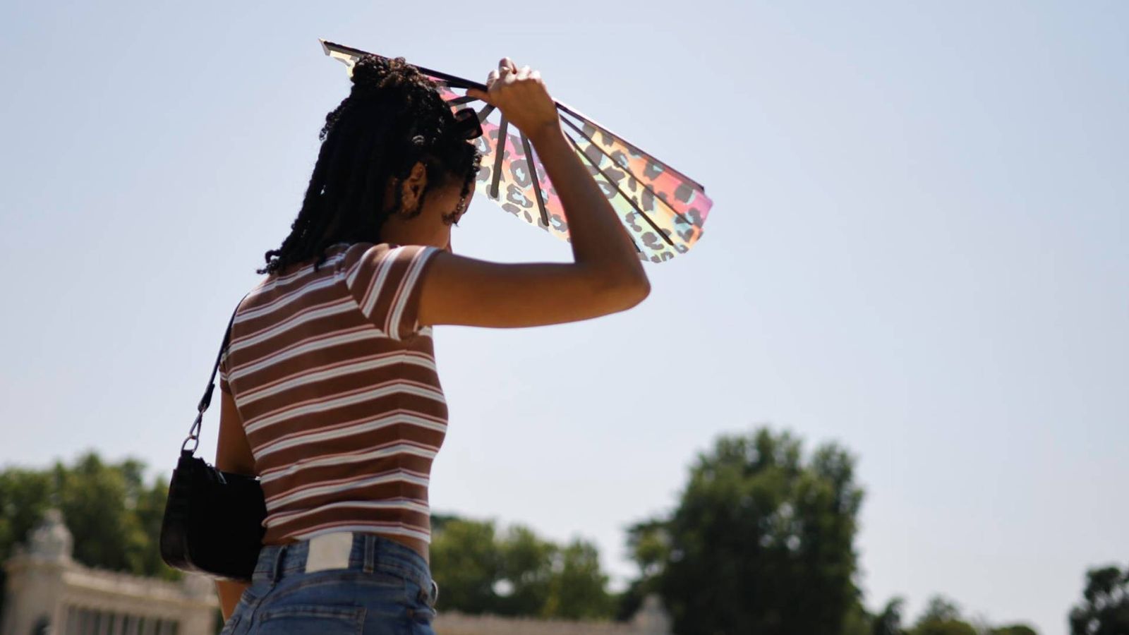 Una chica se protege del sol con un abanico en el parque de El Retiro de Madrid