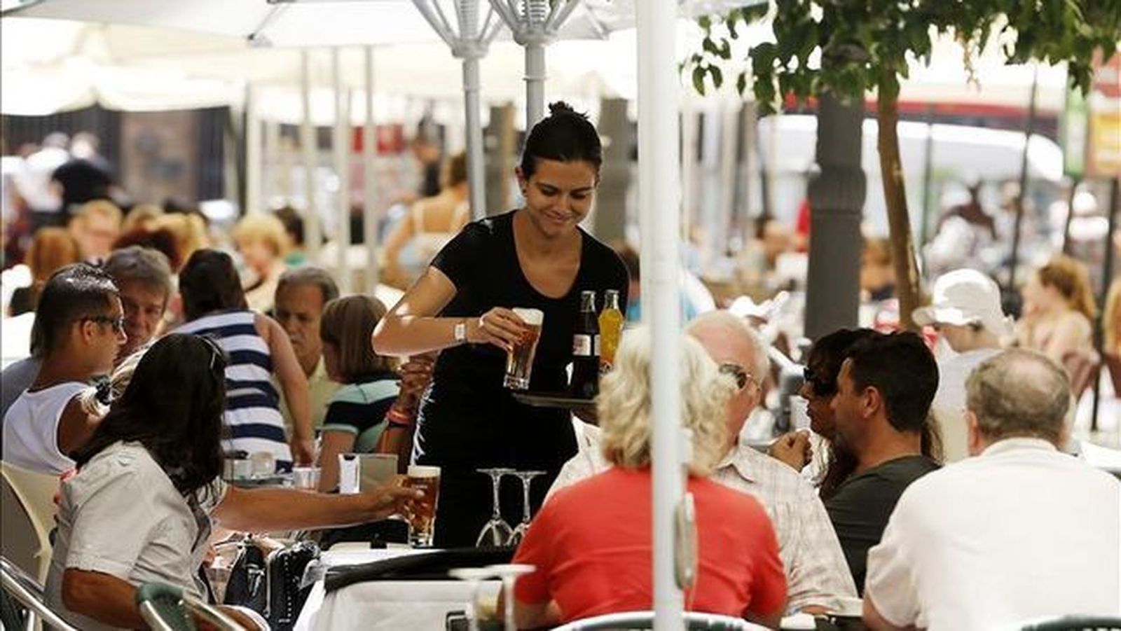 Una camarera sirve a unos turistas en la terraza de un restaurante