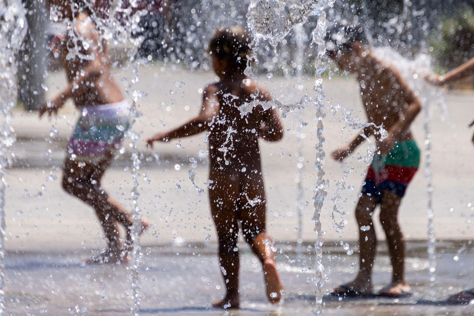 Unos niños se refrescan en unos chorros de agua
