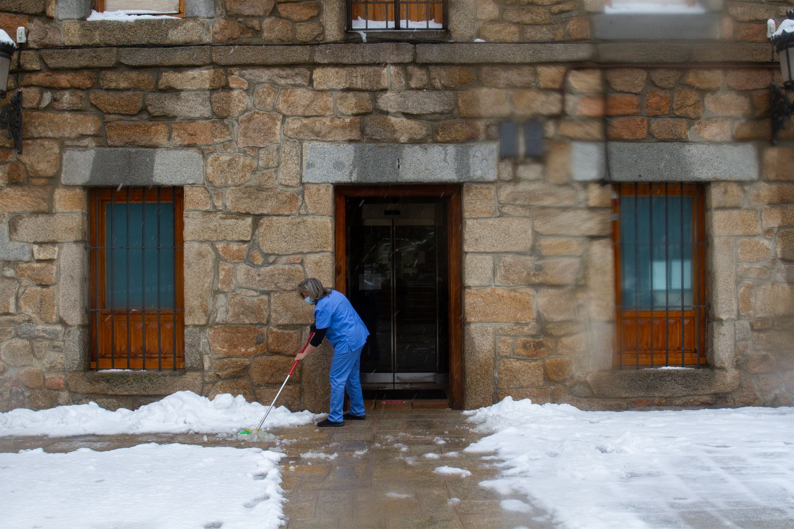 Una mujer despeja la nieve de la entrada del Ayuntamiento de Navacerrada