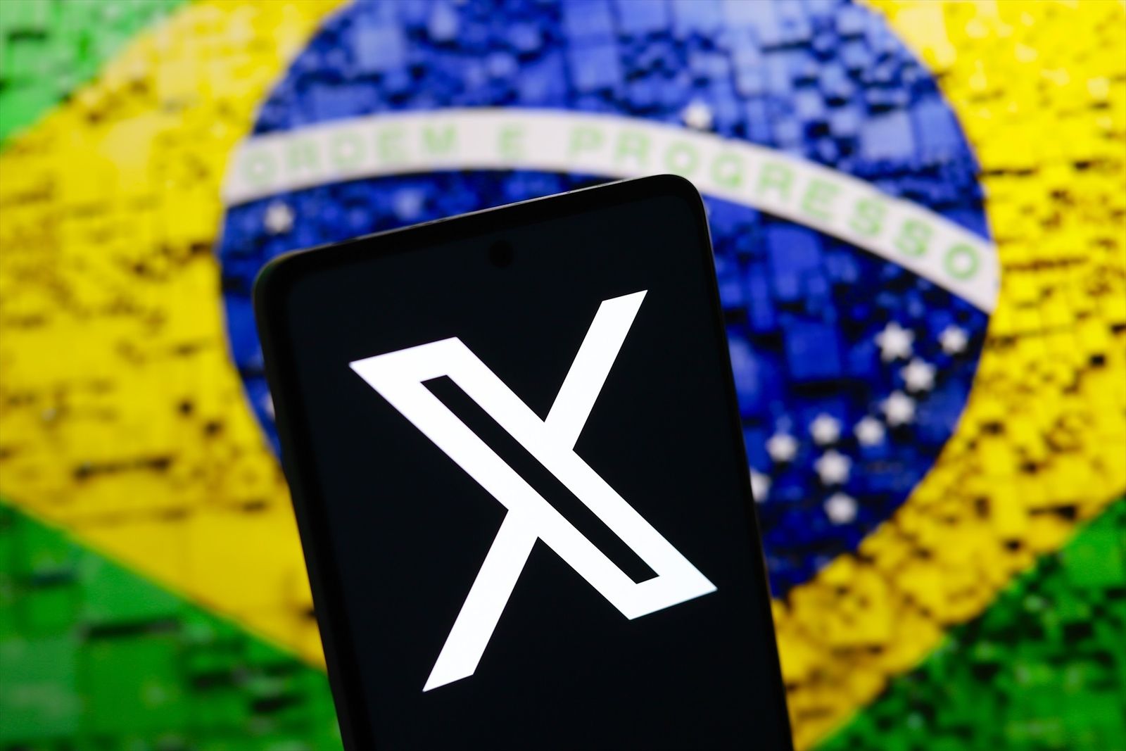 El logo de la red social X en un teléfono móvil frente a la bandera de Brasil
