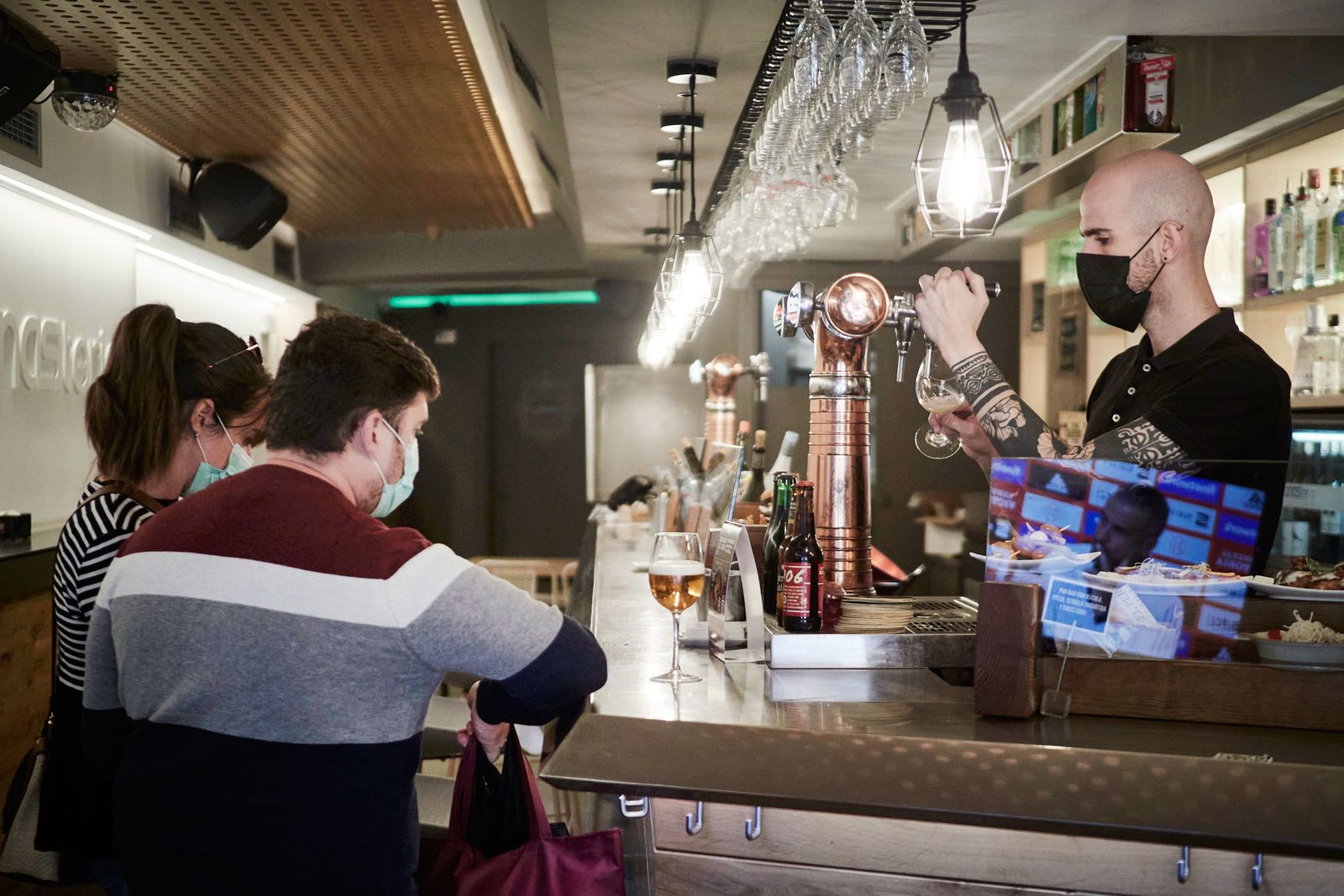 Los clientes y el camarero de un bar se protegen con mascarillas en el interior del establecimiento