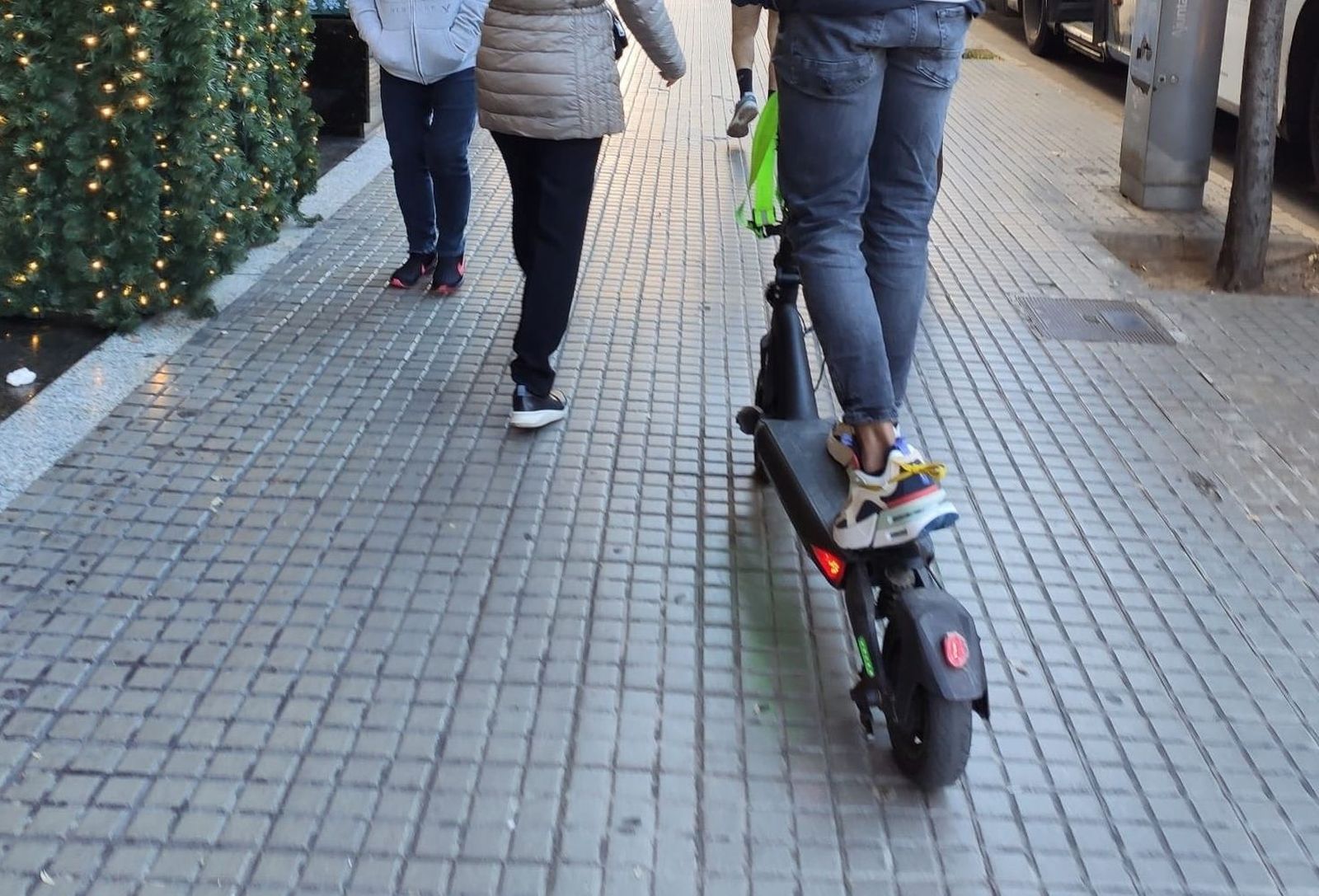 Una persona conduce un patinete por la acera entre peatones