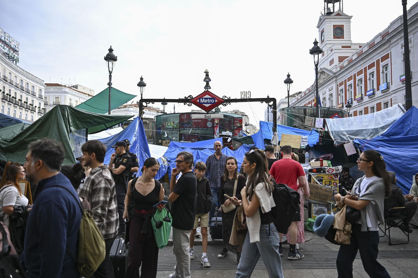 Varias personas salen de la estación de metro en la Puerta del Sol que continua rodeada de tiendas de campaña