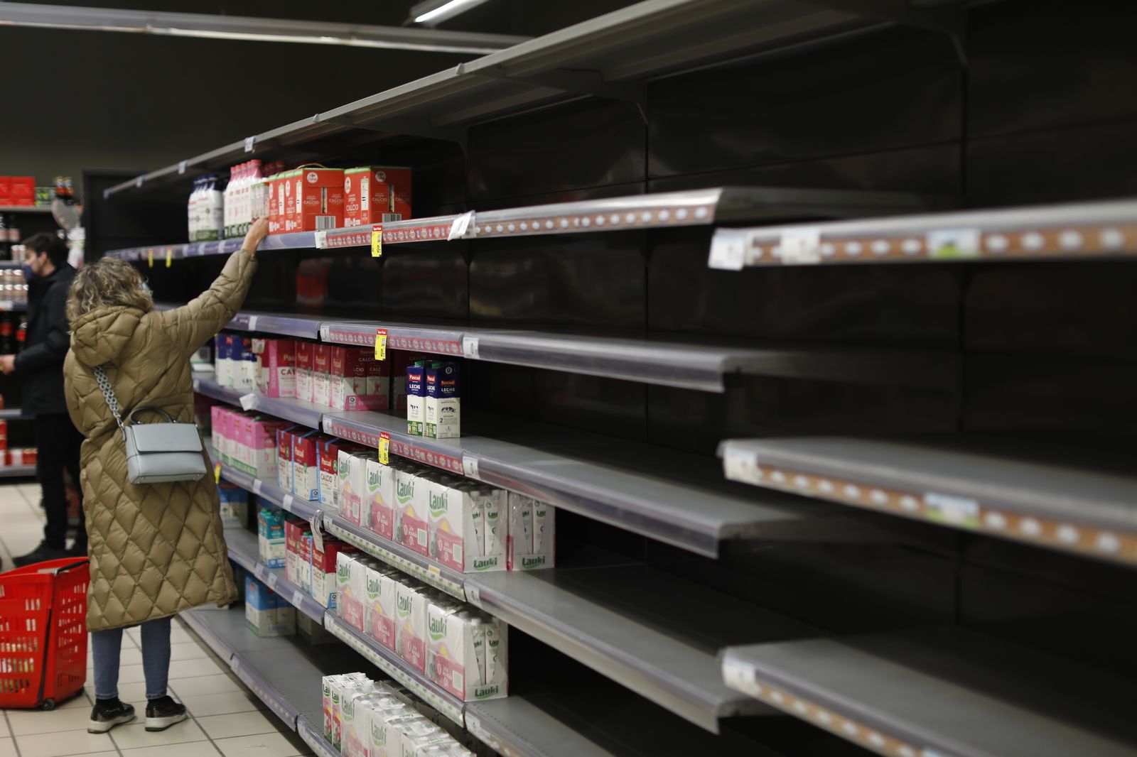 Una mujer frente a la estantería de leche que le faltan algunos productos, en un supermercado Carrefour de Madrid