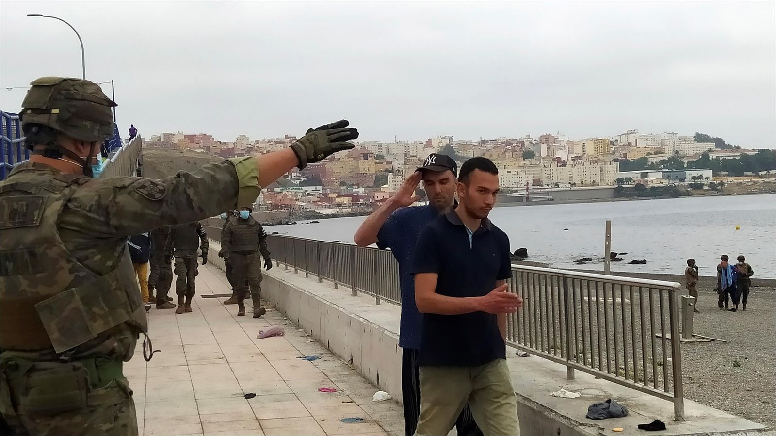 Un miembro del Ejército de Tierra da instrucciones a un grupo de inmigrantes en uno de los espigones fronterizos de Ceuta