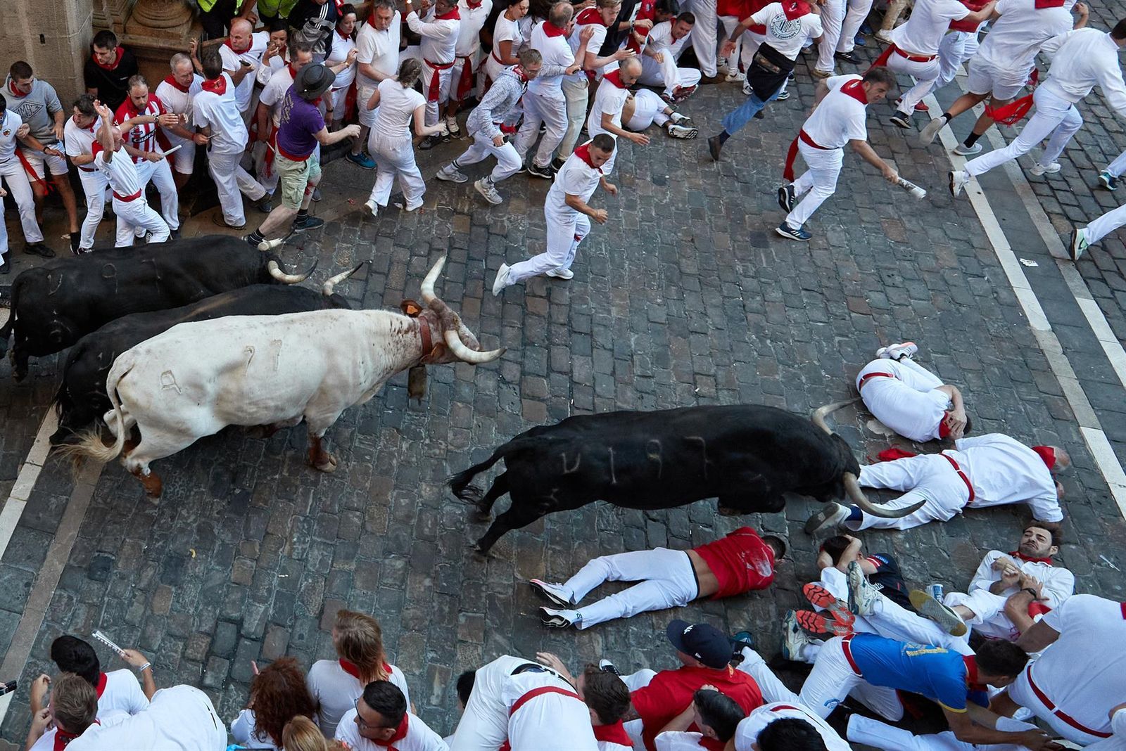 Varios mozos caen ante los toros de la ganadería gaditana de Fuente Ymbro al final del tramo de la cuesta de Santo Domingo durante el segundo encierro de los Sanfermines 2022,