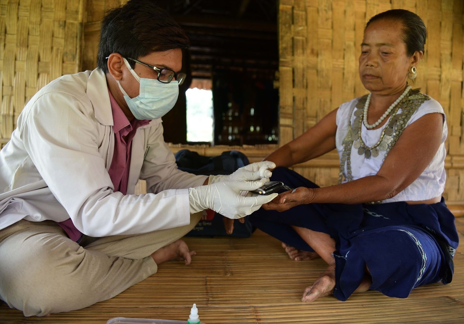 Un médico realiza una prueba de malaria a una mujer de la tribu reang en su choza de bambú en el pueblo de Birendranagar