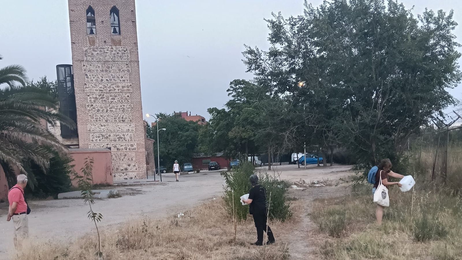 Varias personas riegan los árboles próximos a la Ermita de Santa María La Antigua, en Carabanchel