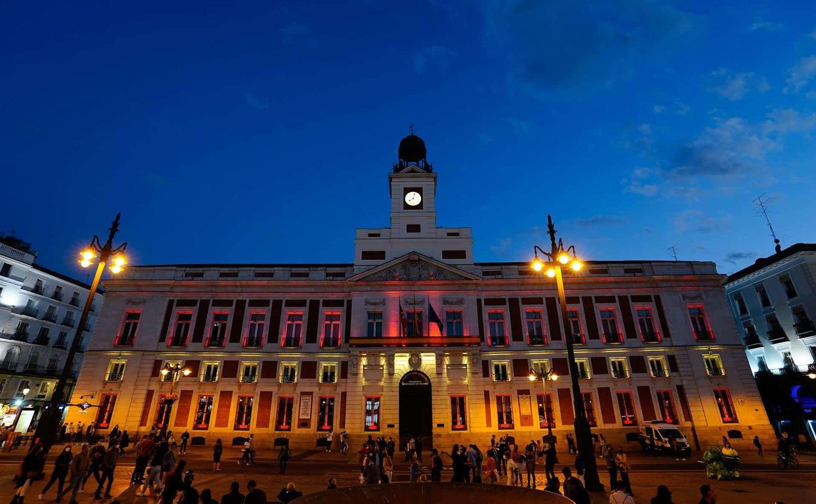 Fachada iluminada de rojo y gualda de la Real Casa de Correos de Madrid, sede del Gobierno regional
