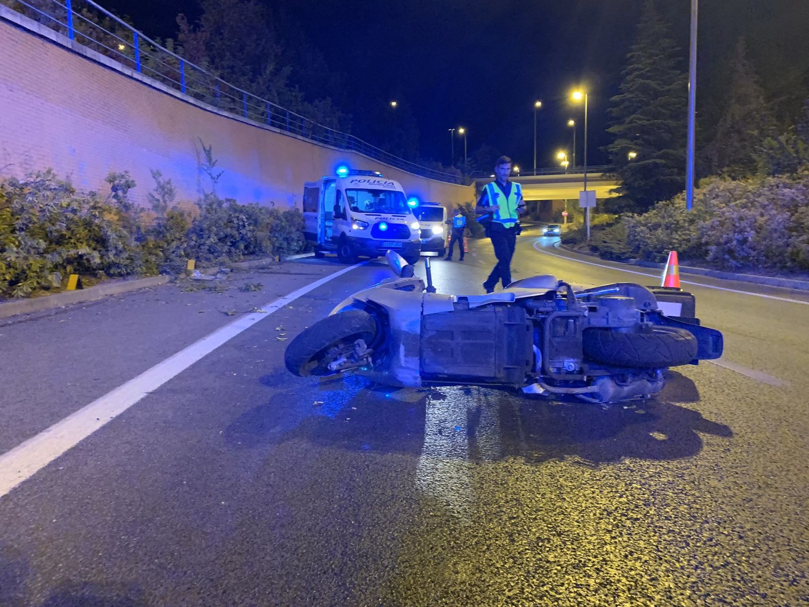 Agentes municipales en el lugar del accidente con la moto siniestrada en primer plano