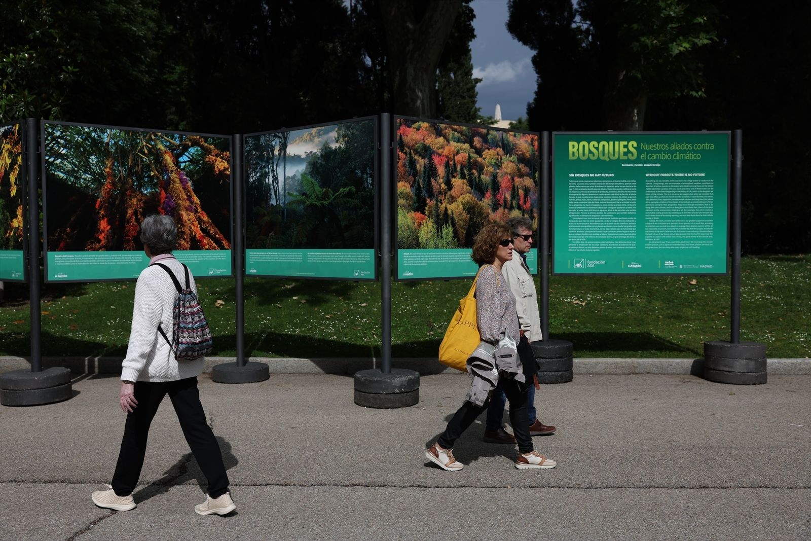 Varias personas pasan por delante de la inauguración de la exposición fotográfica 'Bosques, nuestros aliados contra el cambio climático', 'Casa de Fieras' del Retiro, 30 de mayo de 2023, en Madrid (España)