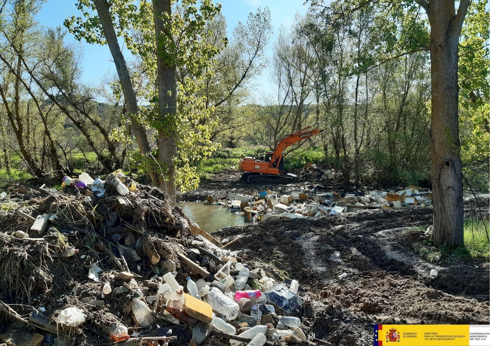 Una excavadora retira montones de basura acumulados en el cauce y las orillas del Guadarrama