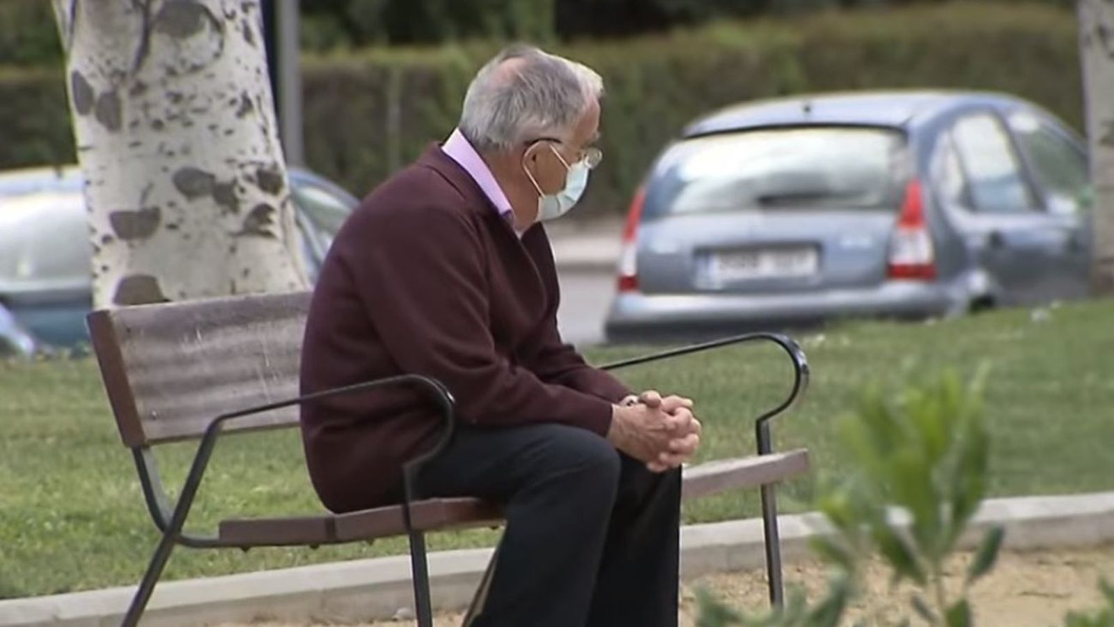 Una persona mayor, sola, sentada en un banco en la calle