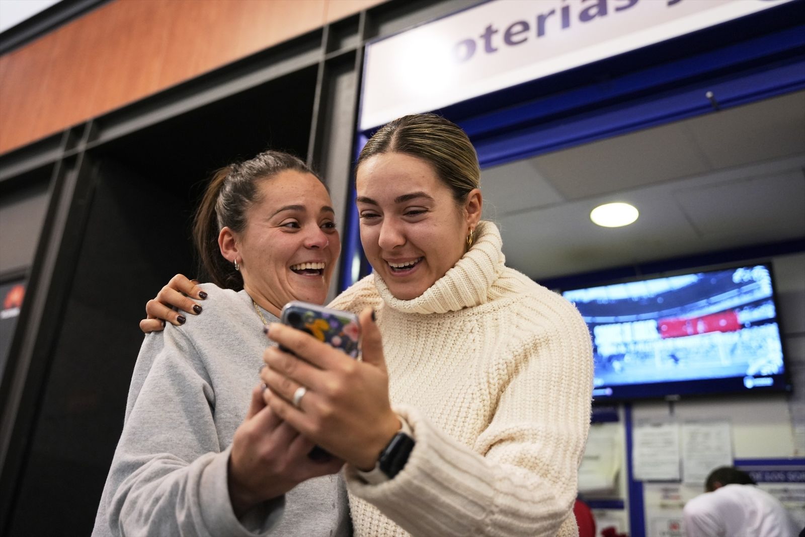 Dos personas sonríen ante un móvil delante de una administración de lotería