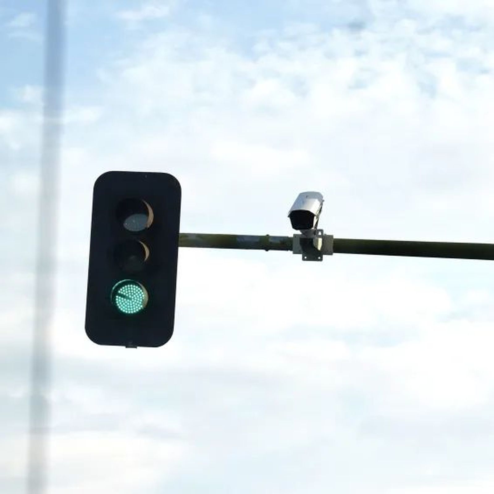 Un semáforo en fase de verde con una cámara de control de tráfico