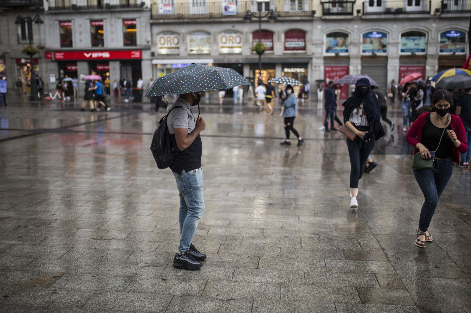 Varias personas se protegen de la lluvia en la Puerta del Sol