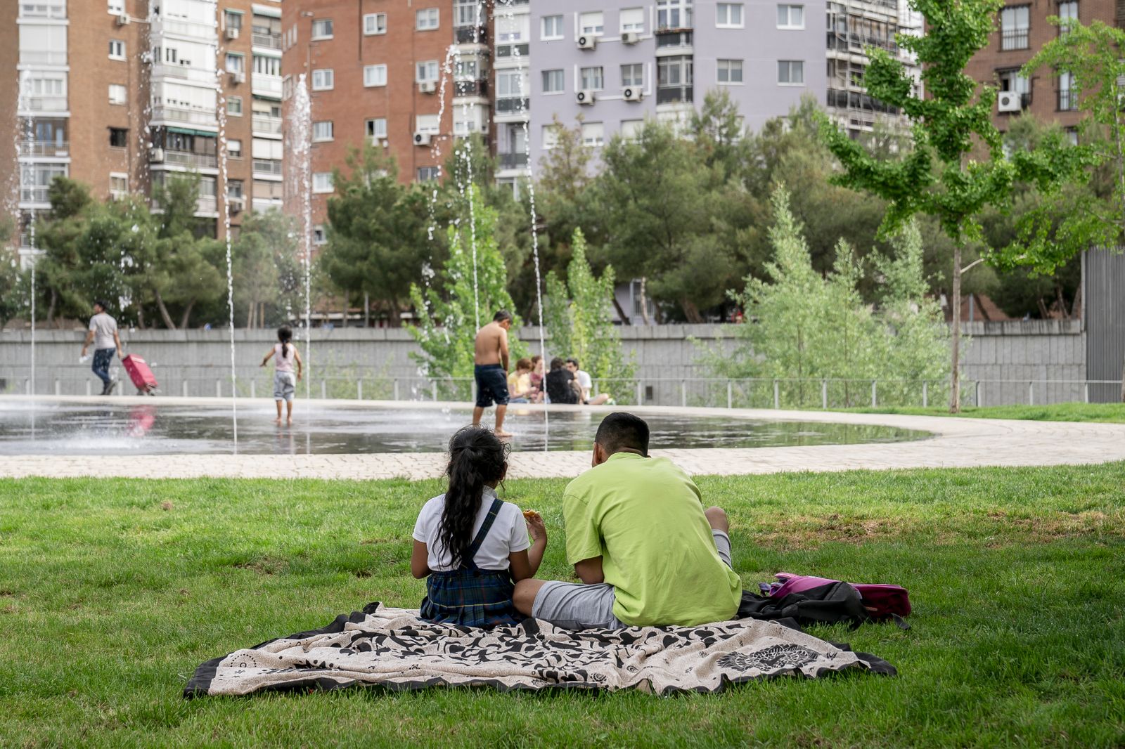 Una niña y un hombre descansan en el césped frente a la playa de Madrid Río