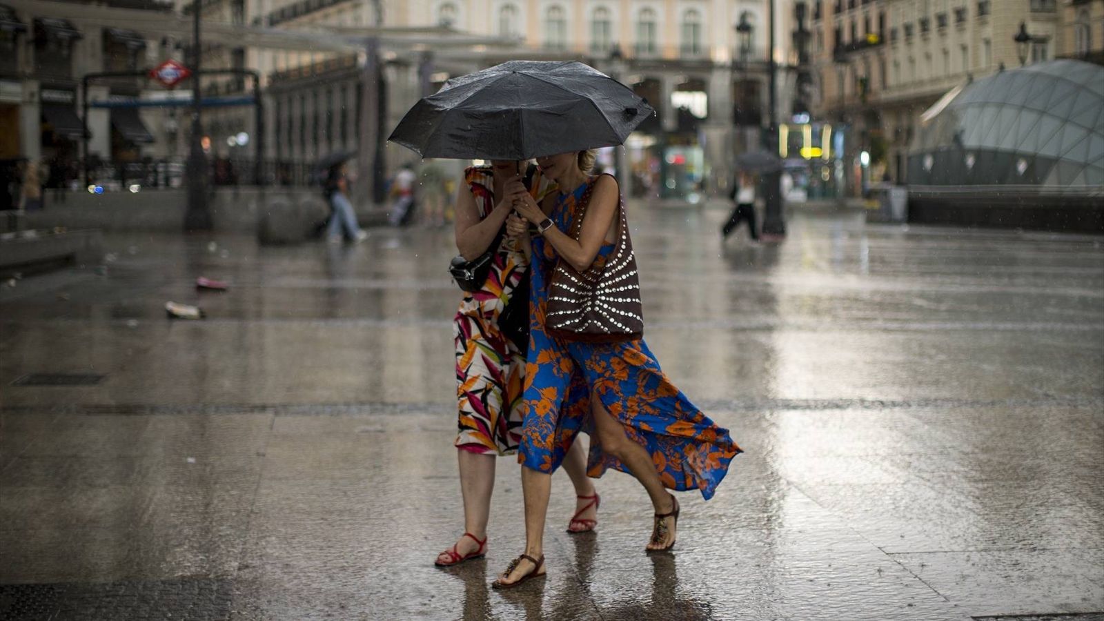 Dos mujeres se cubren de la lluvia con un paraguas en la Puerta del Sol de Madrid
